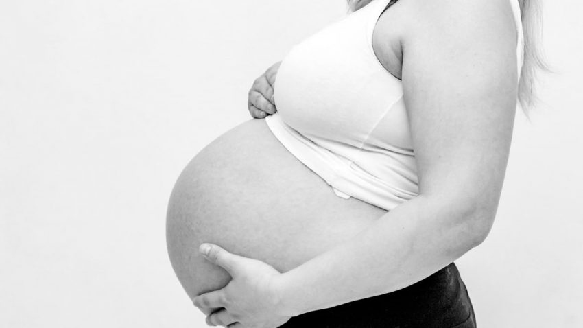 Black and white close-up of a pregnant woman's belly, highlighting maternity and motherhood.